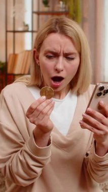 Genç yetişkin bir kadın evde kanepede oturmuş endişeli yüzüyle akıllı telefona bakıyor ve kripto para biriminin düşüşünü izliyor. Kız hayal kırıklığı içinde başını sallıyor, başarısız yatırım kaybına duygusal hayal kırıklığına tepki veriyor.