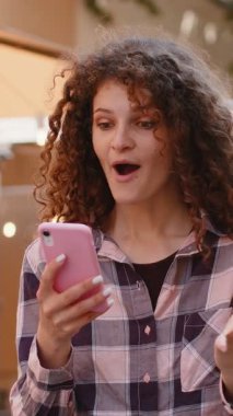 Aman Tanrım. Vay canına. Heyecanlı neşeli kazanan güzel genç bayan akıllı telefon daktilo kullanıyor kutlama yapıyor iyi haber kazan. Cep telefonlu bir kadın şehir güneşli caddede yürüyor.