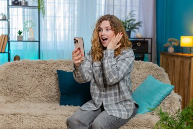 Evde cep telefonunu kaydıran genç bir kadın, haber, indirim ya da Kafkasyalı bayanı temsil eden kazanan sonuç için heyecanlanıyor. Kanepedeki kızıl saçlı kız haykırıyor. Şaşırmış, sevinçli bir kutlama reaksiyonu gösteriyor.