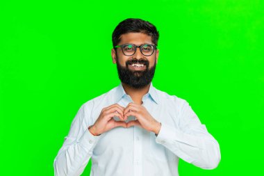 Hintli bir adam kalp şeklini alır. Elleri göğsüne yakındır. Nazikçe gülümser. Yeşil krom anahtar arka planında izole edilmiş Arap bir adam duygusal mesaj gösteriyor.