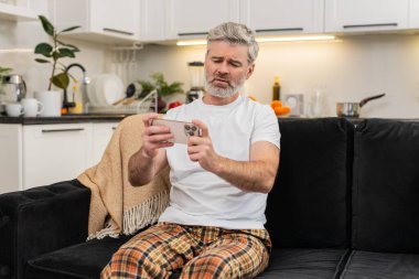 Evde orta yaşlı bir adam akıllı telefondan oyun oynamayı kaybediyor ve piyango uygulamasının kötü sonuçlandığını görüyor. Kanepedeki olgun adam tekrar dene şans için kumarhane umutları başarısız nefesler ağır eller titrek bakışlar.