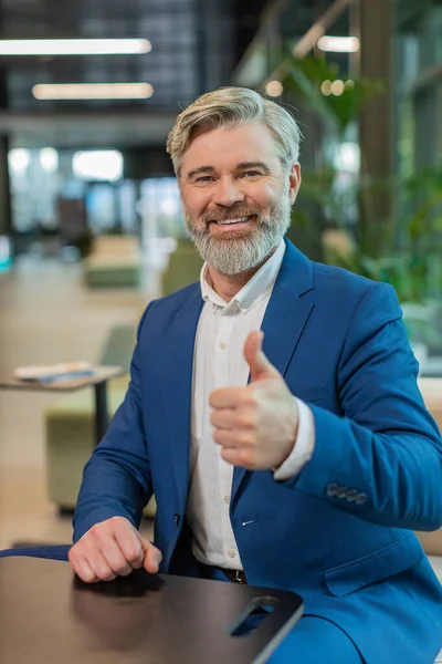 Gibi. Takım elbiseli mutlu, orta yaşlı bir işadamı kameraya bakıp olumlu bir işaret veriyor. Modern ofis lobisinde oturmuş olumlu bir izlenim veriyor. İş insanları.