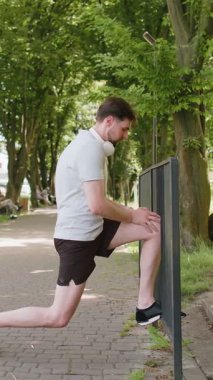 Sportif bir adam kalçalarının ve kalçalarının kaslarını güçlendirmek için tek bacakla hamle yapıyor. Sağlıklı yaşam tarzı ve açık hava eğitimi. Spor salonundaki adam hiçbir şey yapmıyor. Şehir parkında spor aktivitesi.