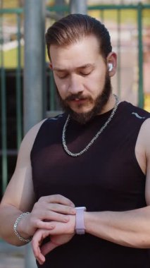 Spor giyimli atletik Lübnanlı adam akıllı saat kullanıyor, kulaklıkla müzik dinliyor. Orta Doğulu gülümseyen genç çocuk oyun alanında çalışıyor. Kalp atışları kontrol ediliyor, başvuru için rota