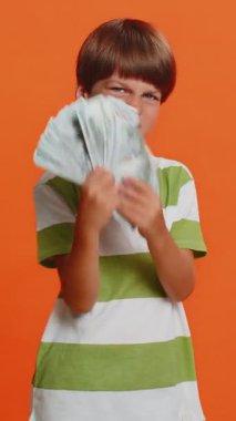 Zengin, mutlu, çocukluk çağındaki genç bir çocuk hayran, başarı işi, piyango kazananı, büyük gelir kaynağı gibi para dolar banknotları sallıyor. Turuncu arka planda izole edilmiş küçük çocuklar