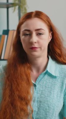 Memnun olmayan kızıl saçlı bir kadın nahoş berbat bir fikre tepki veriyor, kötü kaliteden memnun değil, el sallıyor, başını sallıyor. Evdeki kanepede oturan kadın.