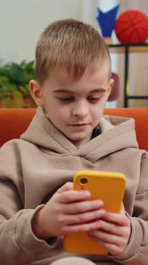 Mutlu çocuk cep telefonu daktiloyla yazı yazarak büyük bir sürpriz buldu, iyi haberler, online maç kazancını kutladı. Erkek ergen çocuk evde oturma odasında kanepede oturuyor.