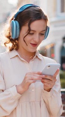 Kablosuz kulaklıklar takmış, açık havada dans eden ve en sevilen disko rock 'n roll müziğini dinleyen mutlu, gevşemiş genç kadın. Şehir güneşli sokaklarında yürüyen kadın