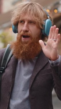 Kablosuz kulaklıklı, neşeli sakallı mutlu genç adam dışarıda akıllı telefondan dans ederek en sevilen disko rock 'n roll müziğini dinliyor. Şehir caddesinde yürüyen turist çocuk.