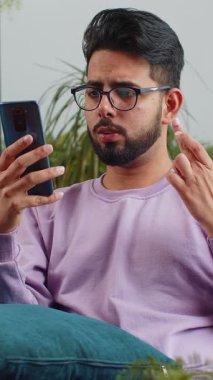 Üzgün Hintli adam akıllı telefon daktilo kullanıyor. Ani piyango sonuçlarını kaybediyor. Kötü haber, servet kaybı, başarısızlık, teslim tarihi, virüs. Genç Hindu çocuk evdeki kanepede oturuyor.