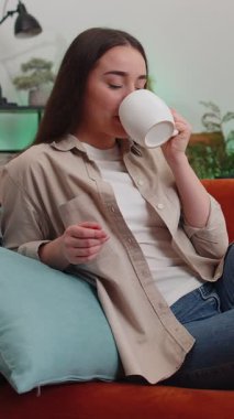 Çekici gülümseyen genç bir kadının portresi bir fincan sıcak kahve ya da kanepede uzanmış bitki çayı içiyor. Oturma odasındaki bayan rahat bir şekilde yalnız başına dinleniyor.