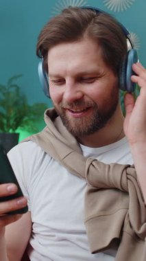 Kablosuz kulaklıklı mutlu beyaz adam evinde koltukta oturup en sevilen enerjik disko dans müziğini dinliyor. İnsanlar hafta sonu boş zaman aktiviteleri