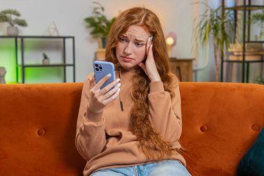 Kafkasyalı, kızıl saçlı, oturma odasındaki kanepede oturan akıllı telefon kullanan mutsuz bir kadın. Günlük giysiler içinde genç bir kız kaybediyor ve piyango ya da kötü haber karşısında şaşırıyor..