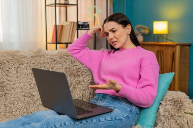 Evdeki genç kadın dizüstü bilgisayar ekranına bakmaktan memnun değil. Üzücü bir ifadeyle baş aşağı duruyor. Kanepede oturan beyaz kız yorgun, iş yükü ve olumsuz duygular yüzünden hayal kırıklığına uğramış.