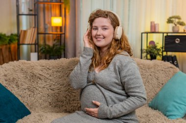 Hamile ve mutlu bir kadın evde kulaklıkla müzik dinliyor, karnına hafifçe dokunuyor, dikkatli adımlarla ve pozitif ruh haliyle dans ediyor. Kız ritimden hoşlanıyor, aşkı, bağlantıyı ve mutluluğu hissediyor..