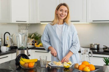 Orta yaşlı kadın mutfaktaki yeşil smoothie için karıştırıcıya muz, ıspanak, spirulina klorella ve su ekliyor. Genç kız evde keto diyeti ve vitaminler için sağlıklı detoks içeceği fikrinin keyfini çıkarıyor..