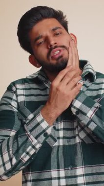 Diş ağrısı ve diş eti iltihabından muzdarip yaralı yanağa dokunan Hintli sakallı adam dişçi randevusu diş eti hastalığını bekliyor. Yakışıklı Hindu çocuk bej arka planda kapalı stüdyo çekimleri yapıyor.