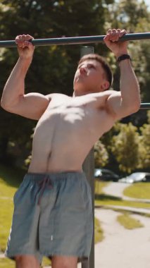 Beyaz tenli, üstsüz, kaslı bir adam yatay barda barfiks egzersizi yapıyor. Genç bir çocuk yaz parkında sırt kaslarını şişiriyor. Spor sağlık programı, antrenman. Güç, motivasyon.