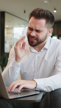 Ofis lobisindeki beyaz iş adamı dizüstü bilgisayarla çalışıyor ve diş ağrısının ağıza dokunduğunu hissediyor. Diş hastalığından dolayı acı veren bir ifade. Pulpitis, sakız hastalığı, diş hastalıkları konsepti.