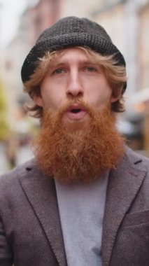 Aman Tanrım, vay canına. Genç sakallı adam kameraya şaşkın şaşkın bakıyor, büyük açık gözlerle, ani zafer, oyun kazanma, piyango hedefi başarısı, açık havada iyi haberler. Şehir sokağındaki kızıl saçlı çocuk.