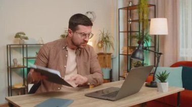 İnternetteki dizüstü bilgisayar aramasında tartışan üzgün işadamı ev ofis masasında rapor çizelgeleri ve grafikler gösteriyor. Genç adam bilgisayar araması sırasında agresif bir şekilde konuşuyor. Stresli serbest çalışan. Tartışma!.