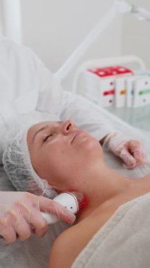 Güzellik uzmanı, kadına yüz ve boyun kaldırma prosedürü yaptırıyor. Kolajen maskesi. Kozmetik uzmanı vakum yüz masajı terapisi için elektrikli ekipman kullanıyor. Cilt bakımı, güzellik tedavisi. Dikey çekim