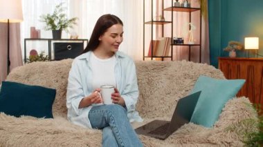 Evde mutlu bir şekilde dizüstü bilgisayarda film seyreden, çay içen, rahatlamış eğlencenin tadını çıkaran genç bir kadın. Kanepede oturan beyaz bir kız kendini rahat hissediyor, duygularını tatmin ediyor, boş zamanlarında pozitif.