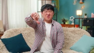 Asyalı adam olumsuz onaylamadığını belirtmek için mutsuz bir ifade sergiliyor. Çinli adam evdeki kanepede oturuyor ve sert bir ifadeyle reddedilme sinyali veriyor.