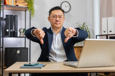 Hoşlanmamak. Merkez ofisteki dizüstü bilgisayarda çalışan Asyalı işadamı hoşnutsuzluğunu ifade eden, memnuniyetsiz kötü işi işaret eden işaret hareketini onayladı. Memnun olmayan Çinli serbest çalışan adam.