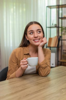 Genç bir kadın sıcak kahve fincanı tutarak evinde oturuyor ve hayatı huzurlu ve mutlu hissederek düşünüyor. Kafkasyalı kız yavaşça nefes alıyor hafif aromanın tadını çıkarıyor ve sakin bir neşe ve minnettarlık anına kucak açıyor.