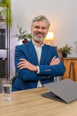 Merkez ofisteki orta yaşlı işadamı dizüstü bilgisayarı kapatıyor. Kollarını kavuşturup projeyi bitirdikten sonra gururla kameraya bakıyor. Masadaki serbest çalışan adam gülümsüyor. Bugün elde ettiği başarıyı yansıtıyor. Kendine güveni tam..