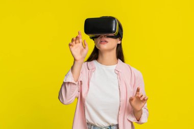 VR kulaklık takan genç bir kadın ellerini havaya kaldırıyor ve sanal dünyaya hayran kalıyor. Sarı arka planda izole edilmiş bir kız dijital deneyime olan hayranlığını ve heyecanını ifade ediyor.