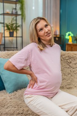 Hamile, orta yaşlı bir kadın belini tutuyor. Omurga incinmesi rahatsızlık veriyor. Kanepede uzanmış beyaz bir kız yavaşça nefes alıyor. Bebek büyümesi sırasında ağrı kesici arıyor.