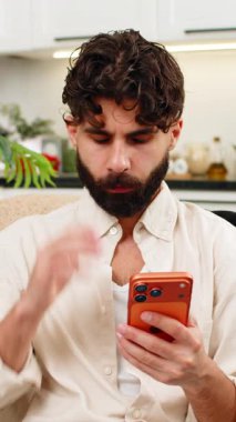 Evdeki Hintli adam akıllı telefona bakıyor online oyun uygulamasında para kaybediyor. Kaybı ve stresi için üzülüyor. Kanepede oturan Arap adam turuncu cep telefonundan kötü haberler okuyor ve hayal kırıklığı yaşıyor.