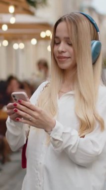 Kablosuz kulaklıklı, neşeli, neşeli genç bir kadın dışarıda dans ederken en sevilen disko rock 'n roll müziğini dinliyor. Şehir caddesinde yürüyen genç bayan.