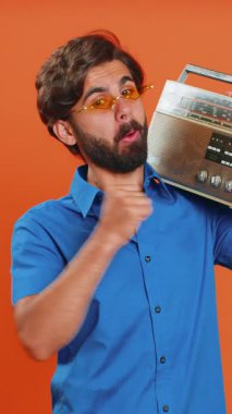 Güneş gözlüklü bir adam müzik dinlemek için retro teyp kullanıyor, favori parçaların disko dansını yapıyor, eğleniyor, eğleniyor, klasik teknolojilerin hayranı. Turuncu arka planda izole edilmiş Arap adam.