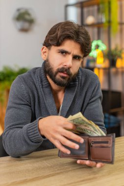 Evdeki Hintli adam cüzdanı açıyor, küçük paralar görüyor, faturalar için endişeleniyor, düşük maaş bütçesi için. Masadaki Arap adam madeni para sayıyor. Maliyet planları harcama kayıtlarını azaltıyor yoksulluk riskini azaltıyor..