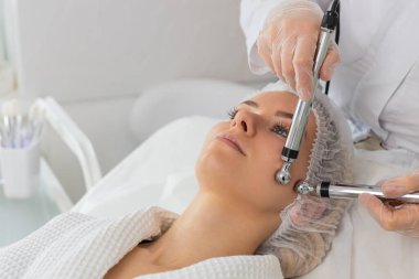 Kozmetik doktoru yetişkin kadınları mikro akıntıya maruz bırakıyor. Yanak terapisi görüyor. Spa kliniğinde anti-yaş kız cilt bakımı. Güzellik uzmanı yüz kozmetik güzellik tedavisi için elektriksel impulslar kullanıyor.