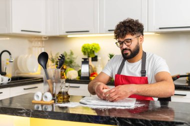 Arap adam mutfakta hamur yoğuruyor kahvaltıda taze pizza ya da börek hazırlıyor. Genç adam ev yapımı hamur işi pişirirken gülümsüyor ve evde sağlıklı konforlu yiyecekler üretiyor..