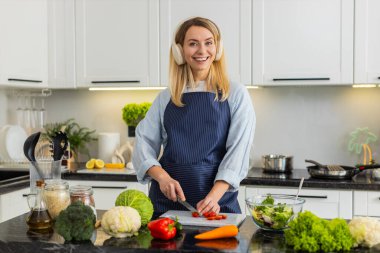 Ev mutfağında müzik dinlerken keto salatası için domates doğrayan orta yaşlı bir kadın. Genç kız sade yemek yaparken rahatlıyor ve kilo kontrolü için sağlıklı beslenme seçeneğini takip ediyor..