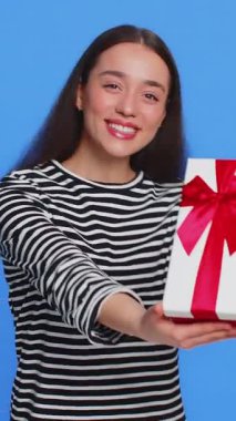 Doğum günü hediyesi sunan olumlu gülümseyen beyaz kadın parti promosyon indirimini kutlamak için hediye paketi uzatıyor. Güzel kız mavi arka planda izole edilmiş