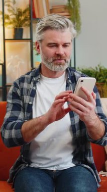 Evdeki koltukta oturan mutlu, olgun bir adam akıllı telefon kullanan eski bir dostundan mesaj alıyor. Gülümseyerek yüzünü yana çevir. Beyaz saçlı, yaşlı bir adam evdeki oturma odasında telefon ekranından iyi haberler okuyor.