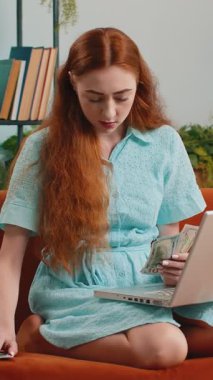 Planlama bütçesi. Zengin, mutlu, kızıl saçlı, nakit sayan ev faturalarını hesaplayan dizüstü bilgisayar kullanan bir kadın. Kazancından memnun olan neşeli bayan, planlı tatil için para biriktiriyor, hediyeler.