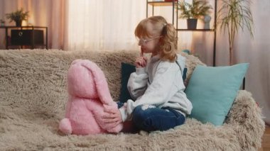 Genç kız evde yumuşak tavşan oyuncağıyla oynuyor, neşeli bir şekilde sohbet ediyor. Kanepedeki sarışın çocuk hayali konuşmaya devam ediyor. Nazik bir şefkatle, tatlı tatlı gülümsüyor..