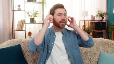 Evde kulaklık takan bir adam garip bir ses duyduktan sonra şaşırmış bir şekilde aniden çıkartıyor. Kanepede oturan beyaz adam gürültüyü tespit etmeye çalışırken merak ve endişeyle tepki veriyor.