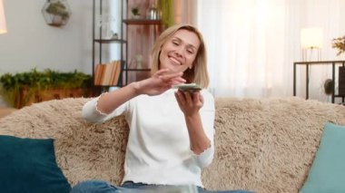 Orta yaşlı bir kadın evdeki koltukta oturup ikramiyeyi kutlarken dolarları başının üstüne atıyor. Yetişkin kadın sevinçle gülümser, finansal başarıyı ifade eder ve mutlulukla duygusal özgürlüğü ifade eder..