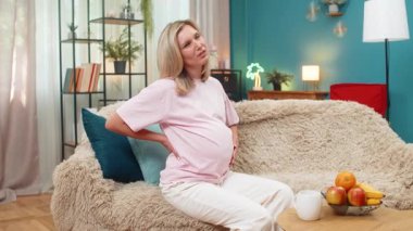 Hamile, orta yaşlı bir kadın belini tutuyor. Omurga incinmesi rahatsızlık veriyor. Kanepede uzanmış beyaz bir kız yavaşça nefes alıyor. Bebek büyümesi sırasında ağrı kesici arıyor.