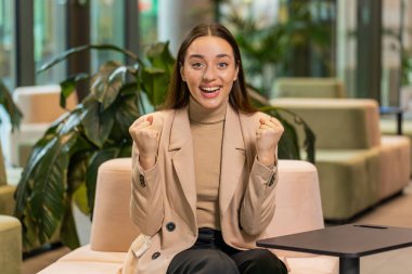 Başarı zaferini kutlayan, kazanan, ofisin lobisinde oturmuş gülümseyen iş kadınının gülümseyen iş kadınının portresi. İş insanları.