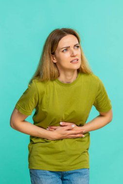 Orta yaşlı bir kadın karın ağrısı çekiyor. Kramplardan, regl ağrılarından ya da kötü yemek tepkilerinden rahatsız olduğunu söylüyor. Mavi arka planda izole edilmiş kız mide ağrısı ya da zehirlenme belirtileri gösteriyor..