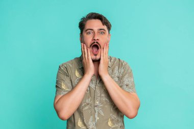 Orta yaşlı bir adam ağzını kocaman açar ve şaşkınlık içinde ellerini yanaklarına bastırır. Beklenmedik bir galibiyete ya da sevinçli bir sürprize tepki verir. Genç yetişkin erkek, mavi arka planda inanılmaz duygusal ve neşeli bir tepki gösterir.